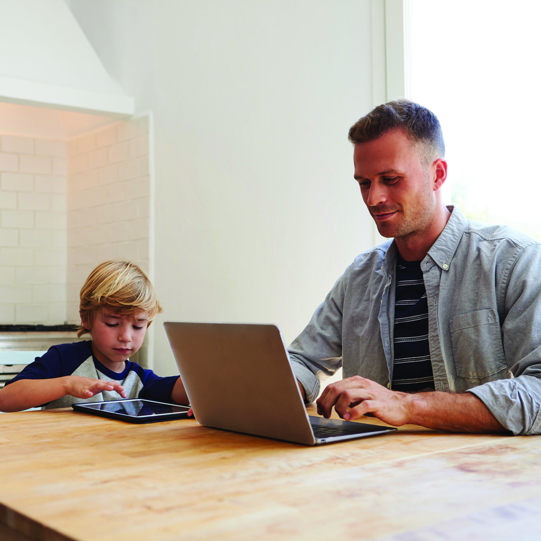 Father and son working on computers at kitchen table 