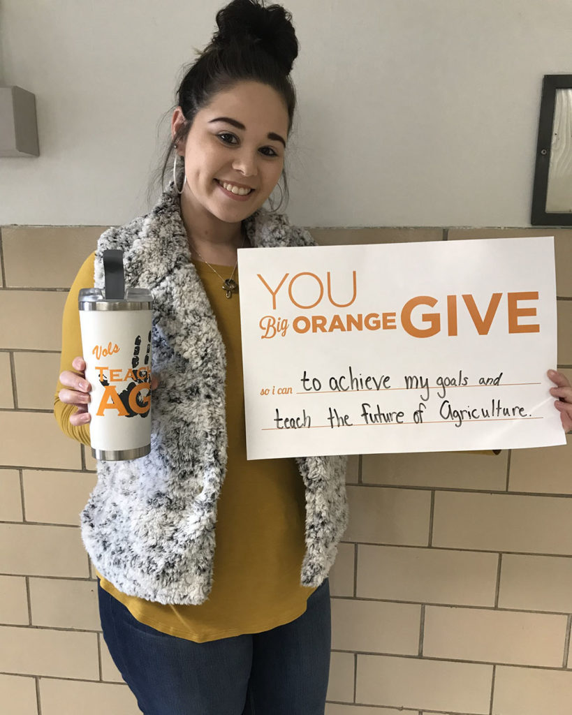 Female student holding a sign that says You Big Orange Give so I can achieve my goals and teach the future of agriculture